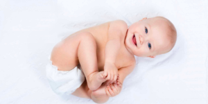 A baby in a diaper touching their toes and smiling up at the camera