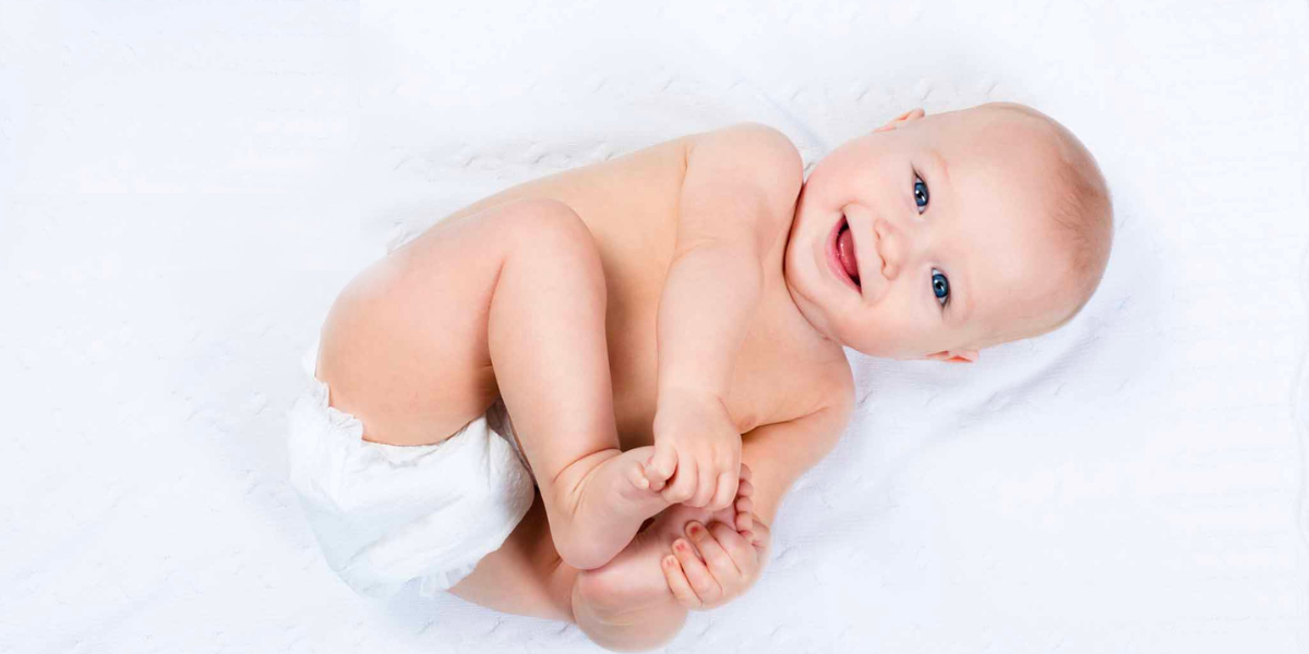 A baby in a diaper touching their toes and smiling up at the camera