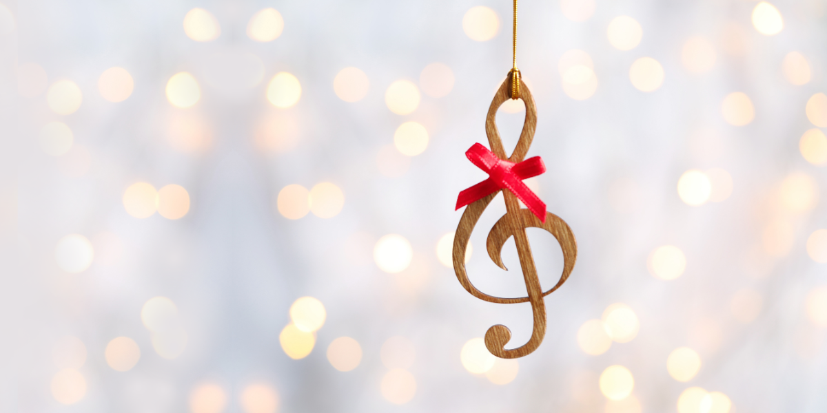 A wooden music note ornament with a red bow on it. The background is white with sparkling Christmas lights