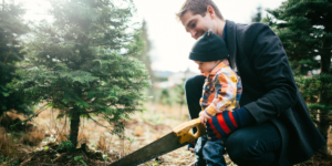 A dad and his toddler son sawing down their Christmas tree