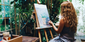 A woman painting plants beautifully. She is also surrounded by tropical plants.